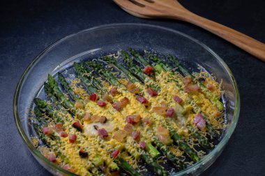 Çedarda pişmiş yeşil kuşkonmaz ve siyah arka planda domuz pastırması.