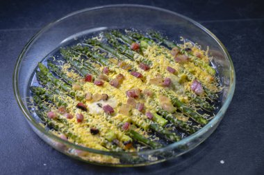 Çedarda pişmiş yeşil kuşkonmaz ve siyah arka planda domuz pastırması.