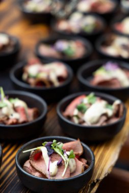 Küçük siyah kâselerde servis edilen soslu ve mikroyeşillikli leziz biftek aperatifleri.