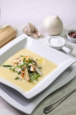 Kremalı patates çorbası, ızgara tavuk, parmesan gevreği ve roka, hafif mermer masa üzerinde malzemeler ve çatal bıçak.