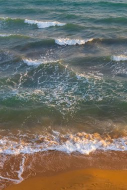 Sakin okyanus dalgaları gün batımında kumlu bir plaja yuvarlanarak sakin ve huzurlu bir atmosfer yaratıyor.