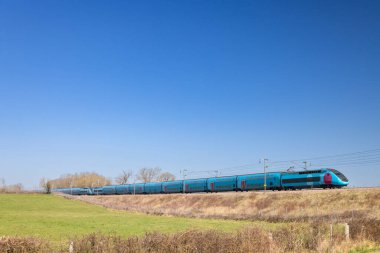 Fransız TGV yüksek hızlı treni açık mavi bir gökyüzü altında kırsalda ilerliyor.