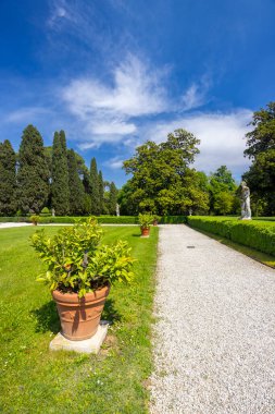 Güneşli bir günde Veneto 'da Palladyan bir villa olan Villa Emo' nun bahçesinden geçen çakıllı yolda heykeller, ağaçlar ve saksılar var.