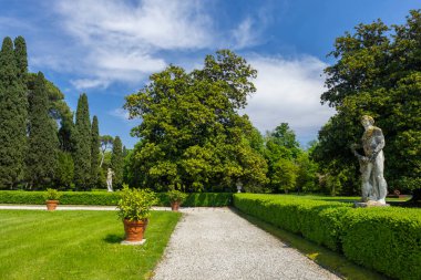 Mavi gökyüzünün altında heykel ve yemyeşil bir bahçe.