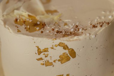 Yenebilir altın yaprağı, beyaz çikolata parçacıkları ve renkli parçalarla süslenmiş kremalı pasta dejenere ve görsel olarak çekici bir ikram sunuyor.