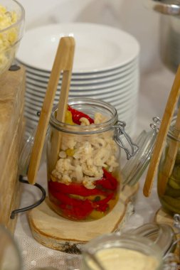 Karnabahar turşulu cam kavanoz ve kışa saklanmış kırmızı dolma biber büfe masasında servis edilir.