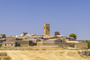 İspanya 'nın Aragon kentindeki büyüleyici bir köy olan Layana' nın panoramik manzarasında tarihi kulesi, geleneksel mimarisi ve ön plandaki altın buğday tarlaları sergileniyor.