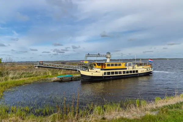 Lauwersmeer Gölü 'ndeki rıhtımdan kalkan sarı yolcu feribotu bulutlu gökyüzü altında, Friesland, Hollanda