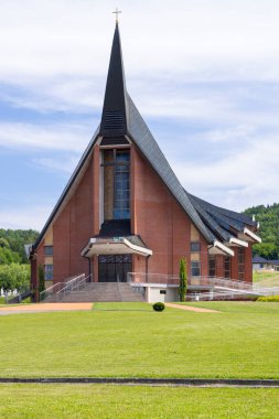 Polonya 'nın Jasienica Rosielna kentindeki yeşil çimlerle çevrili, uzun bir çan kulesi ve haçı olan modern kilise binası.