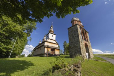 Ladomirova, Slovakya 'daki tahta Katolik Kilisesi mavi gökyüzünün altındaki çimenli bir tepenin üzerinde duruyor.