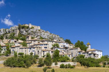Fransa 'nın Provence kentindeki açık mavi gökyüzünün altında ortaçağ şatosuyla kayalık bir çıkıntıya tünemiş Trigance köyünün resimli görüntüsü.
