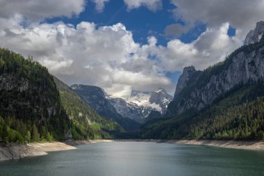 Avusturya 'nın yukarısındaki bulutlu gökyüzünün altında Dachstein Dağları' nı yansıtan Gosaulack 'ı gösteren güzel bir dağlık arazi.
