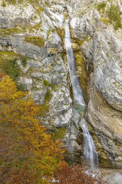 Slovenya 'nın Bovec kentinde renkli sonbahar yapraklarıyla çevrili kayalık bir uçurumdan akan Virje şelalesinin manzarası