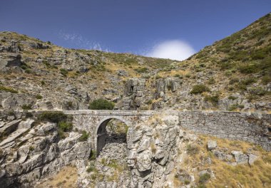 İspanya, Avila 'da, Villarejo del Valle' deki kayalık dağların arasında kurumuş bir nehir yatağını kaplayan antik bir taş köprünün manzarası.