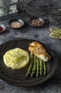 Lezzetli ızgara tavuk göğsü patates püresi ve susam tohumlu kuşkonmaz ile servis edilir. Zarif siyah tabakta.