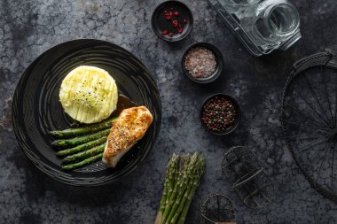 Koyu tabakta patates püresi ve kuşkonmazla servis edilen gurme tavuk göğsü. Sağlıklı ve dengeli bir yemek.