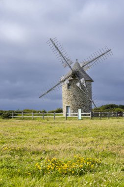 Geleneksel taş değirmeni Cleden Cap Sizun, Finistere, Brittany, Fransa 'da bulutlu bir gökyüzünün altında yeşil bir tarlada duruyor.
