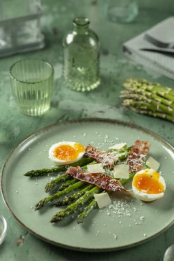 Yeşil tabakta servis edilen yeşil kuşkonmaz, parmesan peyniri ve haşlanmış yumurta, sağlıklı ve lezzetli yemek.