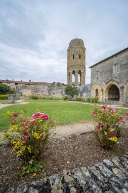 Charroux Abbey Çan Kulesi 'nin manzarası gül çalılarının ve Charroux, Vienne, Nouvelle aquitaine, Fransa' daki yeşil çimlerin üzerinden yükseliyor.