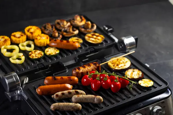 Lezzetli sosisler, sebzeler ve mantarlar elektrikli ızgarada pişiyor.