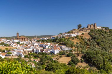 İspanya, Huelva 'daki Cortegana' nın panoramik manzarası, açık mavi gökyüzü altında kale, kilise ve beyaz evleri sergiliyor.