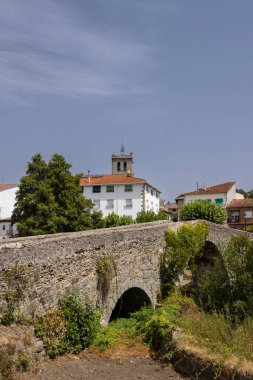 Arenas de San Pedro, Avila, Castilla ve Leon 'da arka planda bir kilise kulesi bulunan küçük bir dereden geçen kemerli eski taş köprü.