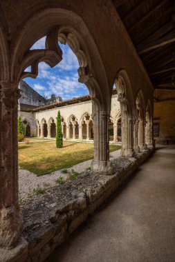La Romieu, Gers, Occitanie, Fransa 'daki Saint Pierre Koleji Manastırı' nın sakin avlu manzarasını çerçeveleyen taş kemerler.