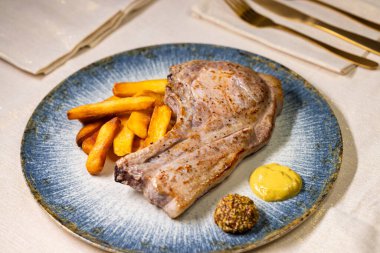 Lezzetli kızarmış domuz pirzolası, patates kızartması ve hardal ile servis ediliyor. Lezzetli ve doyurucu bir yemek için mükemmel.