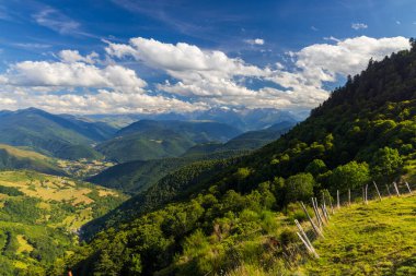Fransa 'daki Pireneler' in göz kamaştırıcı manzarası, bereketli vadiler, uzak tepeler ve tüylü beyaz bulutlarla dolu canlı mavi bir gökyüzü.