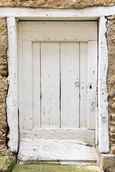 Fransa 'nın başkenti Saint Hilaire' de taş bir duvara döşenmiş, kabuk soyulmuş ve paslı metal donanımlı, beyaz aşınmış ahşap kapı.