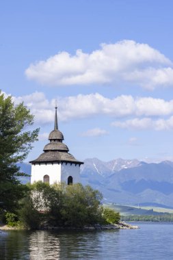 Liptovska Mara Gölü 'nden yükselen ve arka planda görkemli Tatra Dağları olan bir kilise kulesinin resimli görüntüsü, Liptovsky Mikulas Bölgesi, Slovakya