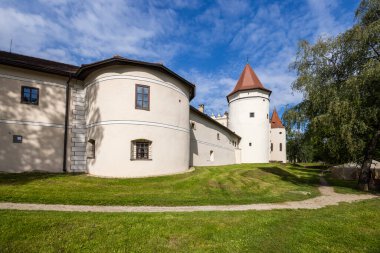 Orta Çağ Kezmarok Kalesi 'nin beyaz duvarları ve kırmızı çatısı Slovakya, Presovsky Kraj' da yeşil çimlerin üzerinde yükseliyor. Mavi gökyüzünün altında bulutlar var.