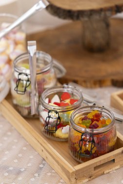 Cam kavanozlar çeşitli renkli şeker ve maşalarla dolu, ahşap tepside dinleniyor, tatlı bir ikram için hazır.