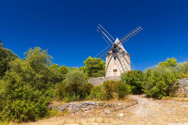 Saint Saturnin les Apt, Provence yakınlarındaki Fransız kırsalındaki ağaçların üzerinde geleneksel yel değirmeni yükseliyor.