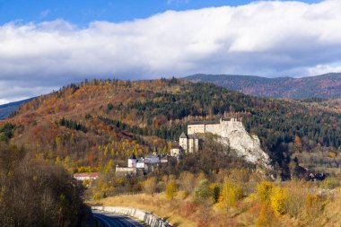 Ortaçağ Oravsky Şatosu güneşli sonbahar gününde renkli ağaçlar ve mavi gökyüzü ile Slovakya 'da beyaz bulutlar
