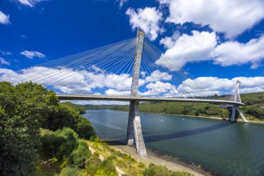 Modern kablo beyaz bulutlarla mavi gökyüzünün altında Argol, Finistere yakınlarındaki Aulne Nehri 'nden geçen köprü olarak kaldı.