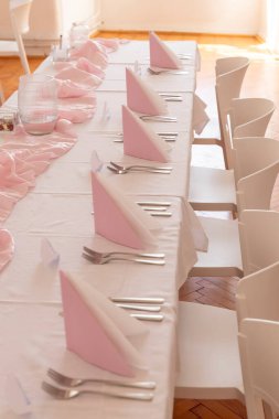 Pembe peçeteler ve çatal bıçak takımı beyaz bir masa örtüsüne dizilmiş. Zarif bir sofra kurun. Misafirleri karşılamaya hazır olun.