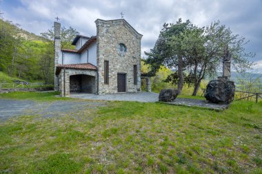 Bulutlu bir günde, Coli, Piacenza, Emilia Romagna, İtalya 'nın yeşil tepelerine bakan heykeli olan küçük taş kilise.