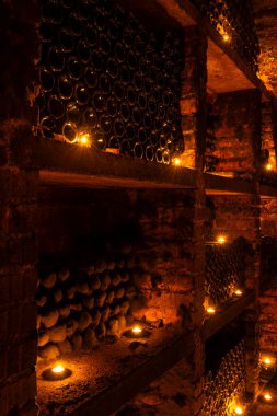 Sıcak mum ışığında karanlık bir mahzende dinlenen tozlu şarap şişeleri canlandırıcı bir atmosfer yaratıyor.