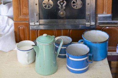 Antika bir sobanın önünde oturmuş, nostaljik bir atmosferi çağrıştıran eski emaye takımları ve fincanlar.