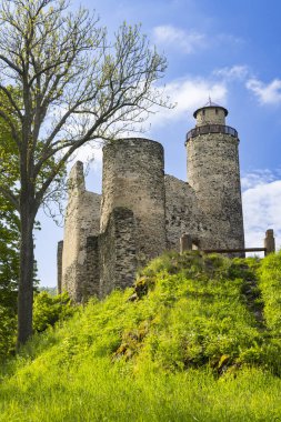 Orta Çağ Kostomlaty kapsülü Milesovkou Kalesi, Çek Cumhuriyeti 'nde beyaz bulutlu mavi bir gökyüzünün altında görkemli bir şekilde duran yeşil bir tepenin üzerinde harabe.