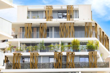 Montpellier, Fransa 'da balkonlarda büyüyen ahşap elementleri ve bitkileri olan modern bir binanın beyaz cephesi