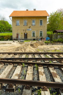 Ustek, Çek demiryolu ve turuncu çatılı eski tren istasyonu binası, rayların arasında inşaat malzemeleri ve bitki örtüsü büyüyor.