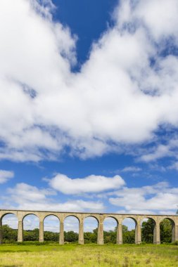 Figeac, Lot, Fransa 'daki antik bir viyadük manzarası, yemyeşil bitki örtüsüyle çevrili, beyaz bulutlarla benekli mavi bir gökyüzünün altında