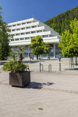 Slovakya 'nın Trencianske Teplice kentindeki modern binanın önündeki meydanda yemyeşil ağaçlar, saksı bitkileri ve kaldırımlar yer alıyor.