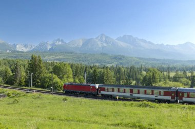 Slovakya, High Tatras 'ın güzel manzarasında Strba yakınlarındaki yolcu trenini çeken kırmızı elektrikli lokomotif.