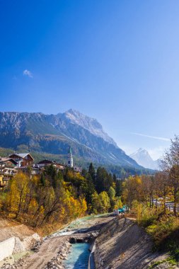 Livinallongo del Col di Lana, Belluno, Veneto, İtalya 'daki renkli ağaçlar, kilise ve dağlarla dolu resimli bir dağ manzarası.