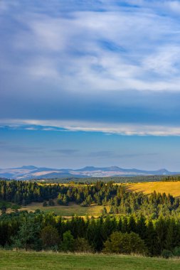 Fransa 'nın Ardeche bölgesinde gün batımının sıcacık parıltısıyla yıkanan yuvarlanan tepelerin, yemyeşil ormanların ve uzak dağların nefes kesici manzarası.