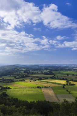 Bulutlu bir gökyüzünün altındaki tarlaların ve tepelerin manzarası