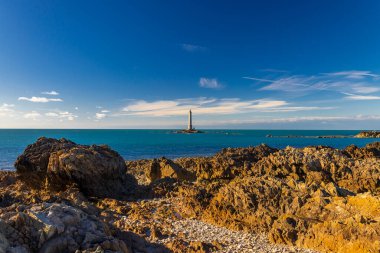 Fransa, La Hague 'de açık mavi gökyüzünün altında kayalık sahildeki deniz feneri